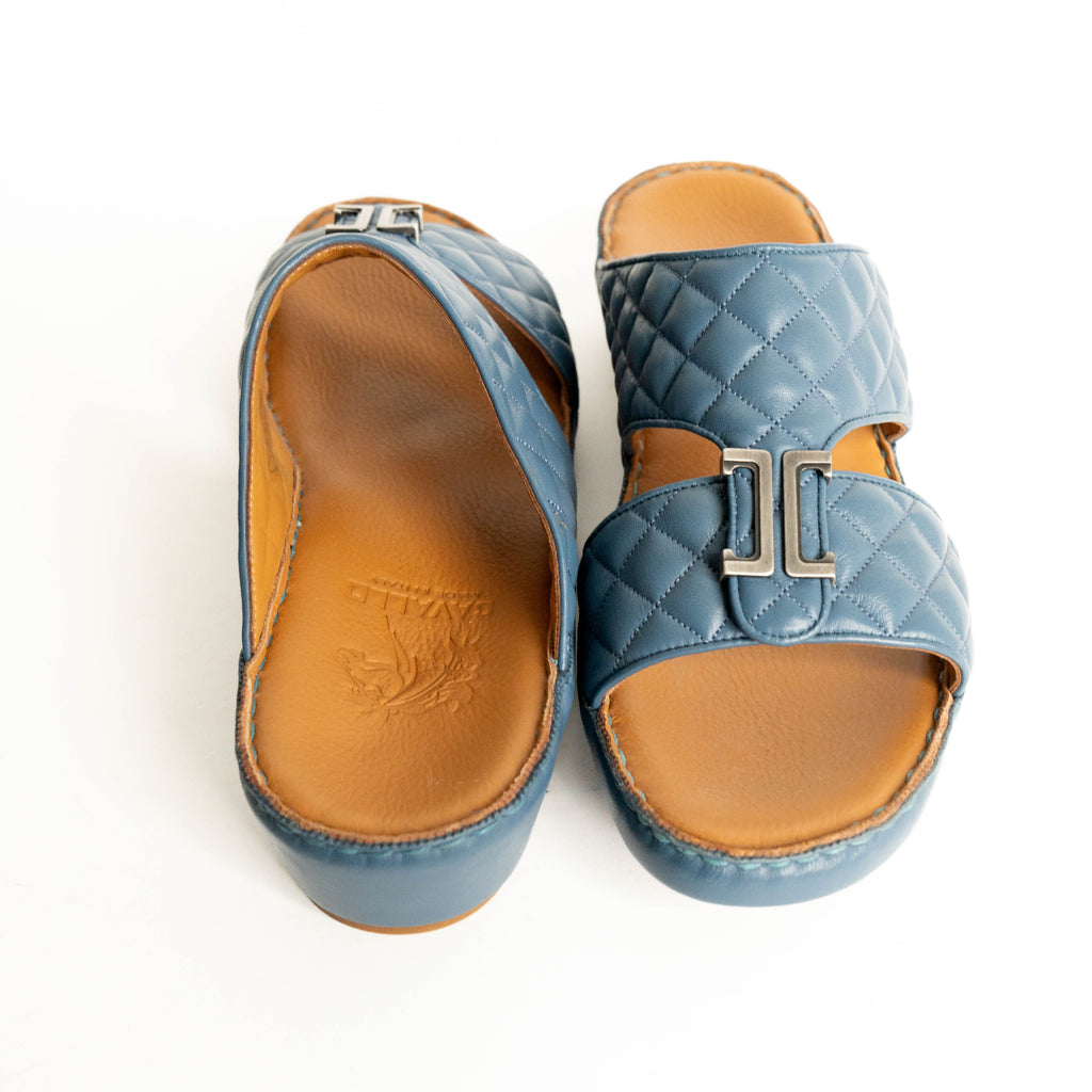Pair of blue quilted sandals with tan soles on a white background