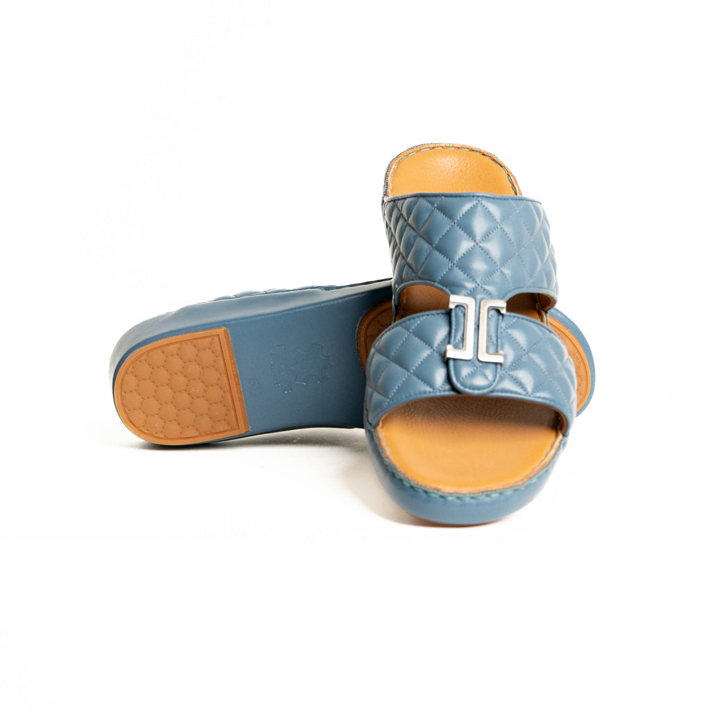 Pair of blue quilted sandals with tan soles on a white background