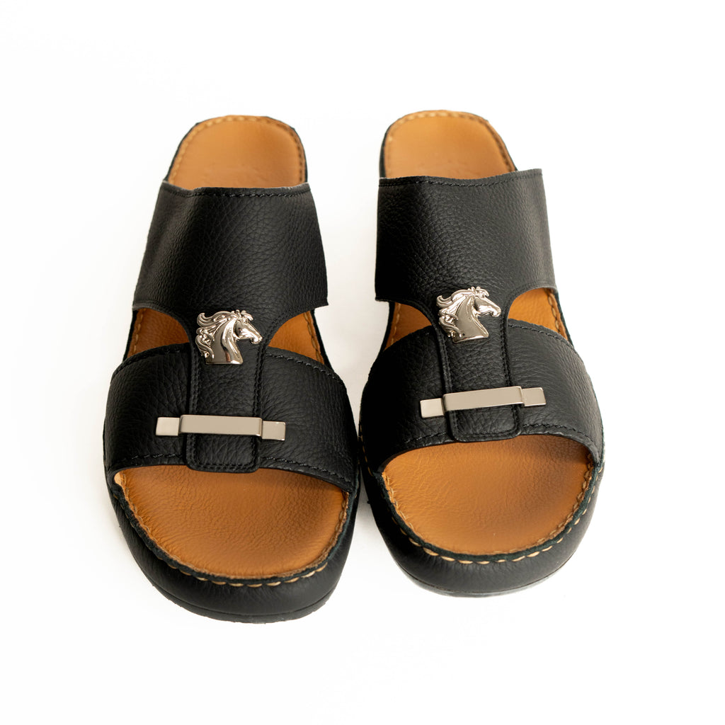 Pair of black and brown sandals with horse buckle design on a white background